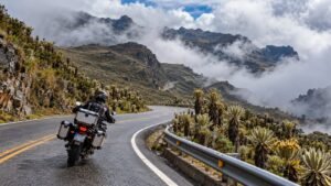 Motorista en una curva de la Carretera Trasandina entre frailejones, con montañas y nubes en el páramo