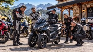 Grupo de moteros mirando con incredulidad un scooter de tres ruedas aparcado frente a una cafetería de montaña